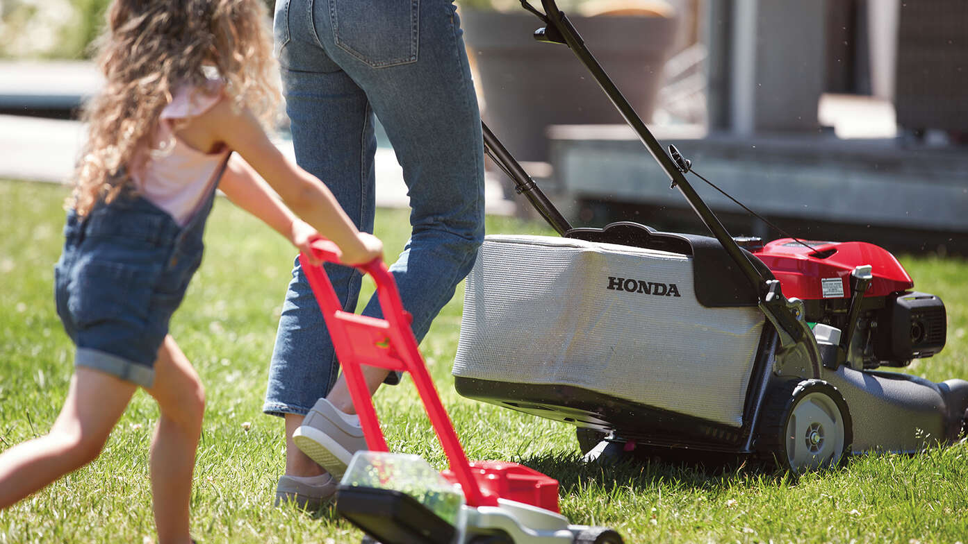Honda IZY Rasenmäher, Seitenansicht mit einer Frau und einem Kind in einem Garten