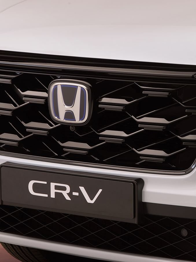 Nahaufnahme des Frontgrills eines Honda CR-V mit schwarzem Wabenmuster, dem Honda-Logo in der Mitte und der Modellbezeichnung CR-V darunter.