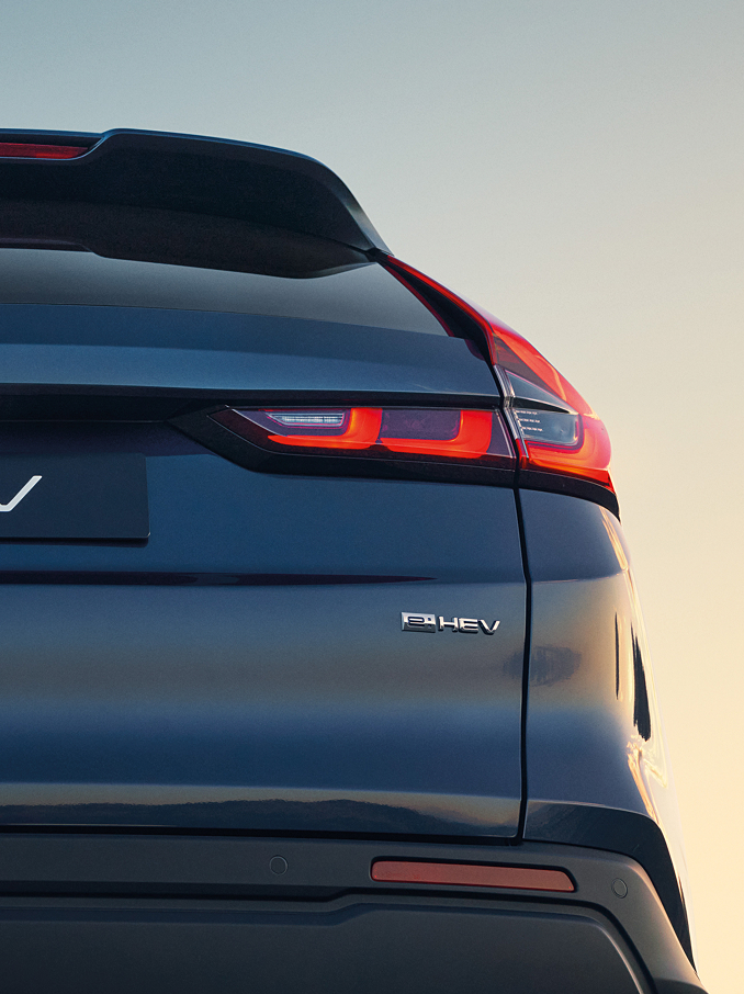 Hecknahaufnahme eines dunkelblauen Honda CR-V e:HEV mit Honda Emblem, CR-V-Schriftzug und beleuchteten Signature-LED-Rückleuchten bei Sonnenuntergang.