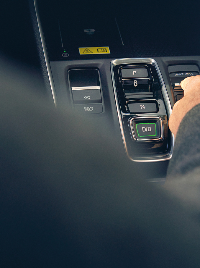 Eine Hand greift nach einem Kippschalter auf der Mittelkonsole eines modernen Autos neben den Gangwahlknöpfen.