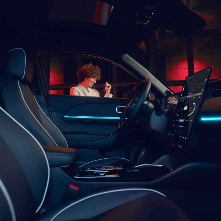 Honda e:Ny1, beleuchteter Innenraum bei Nacht mit Model vor dem Fenster.