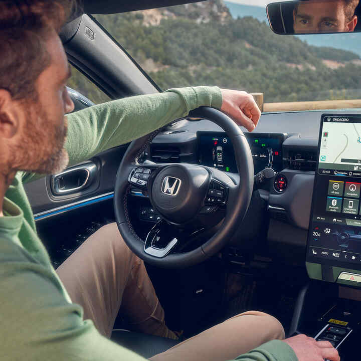 Mann in einem Honda e:Ny1, der das Navigationssystem über das digitale Fahrerdisplay steuert.
