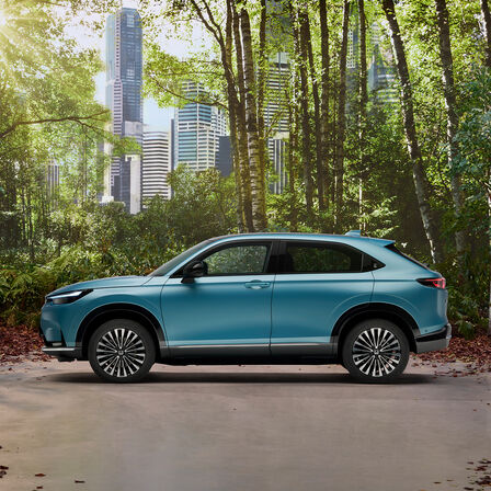 Honda e:Ny1, Seitenansicht im Wald mit einer Stadt im Hintergrund.