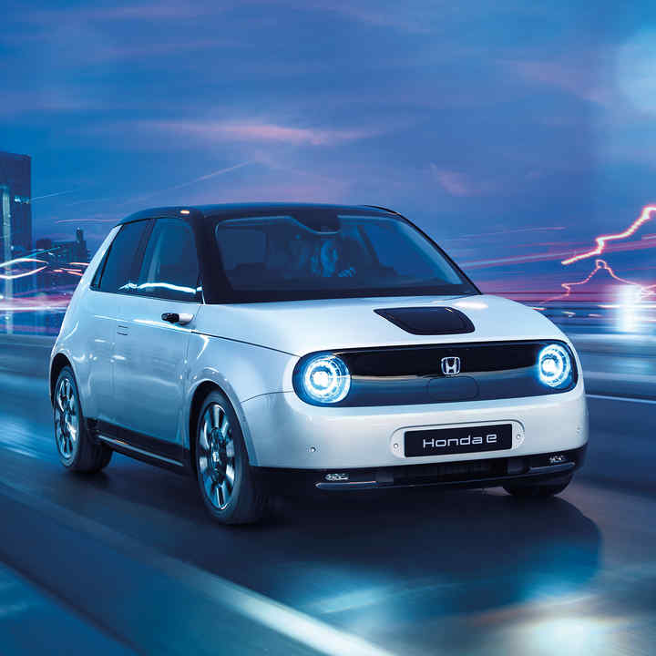 Dreiviertelfrontansicht eines Honda e bei der Fahrt durch eine elektrische Stadtlandschaft.