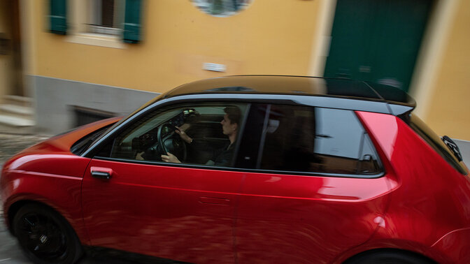 Honda e, 3/4-Frontansicht, beim Fahren durch eine elektrisierte Stadt in der Nacht.