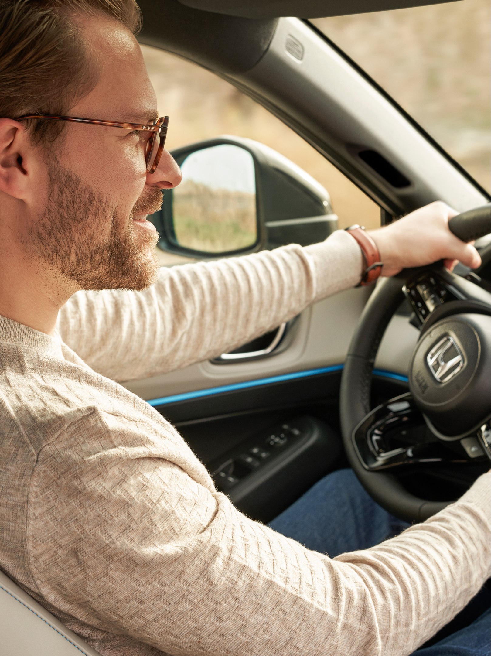 Von der Beifahrerseite aus sieht man einen Mann mit Brille fährt, der einen Honda HR-V fährt, beide Hände am Lenkrad, das Armaturenbrett im Blickfeld.