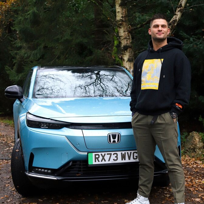 Ein Influencer steht in einem Wald vor einem Honda e:Ny1.