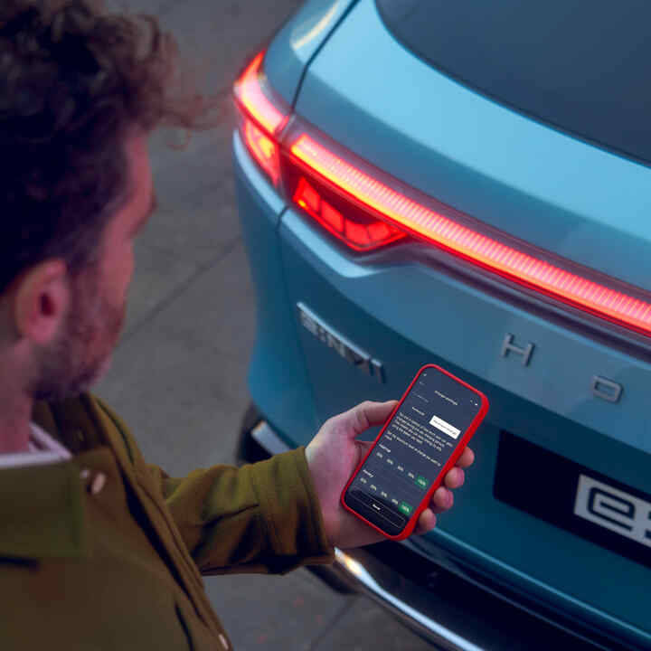 Nahaufnahme einer Person mit Smartphone und My Honda+ App neben einem Fahrzeug