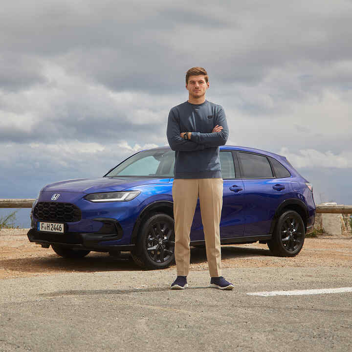 Max Verstappen neben einem blauen Honda ZR-V Hybrid-SUV.