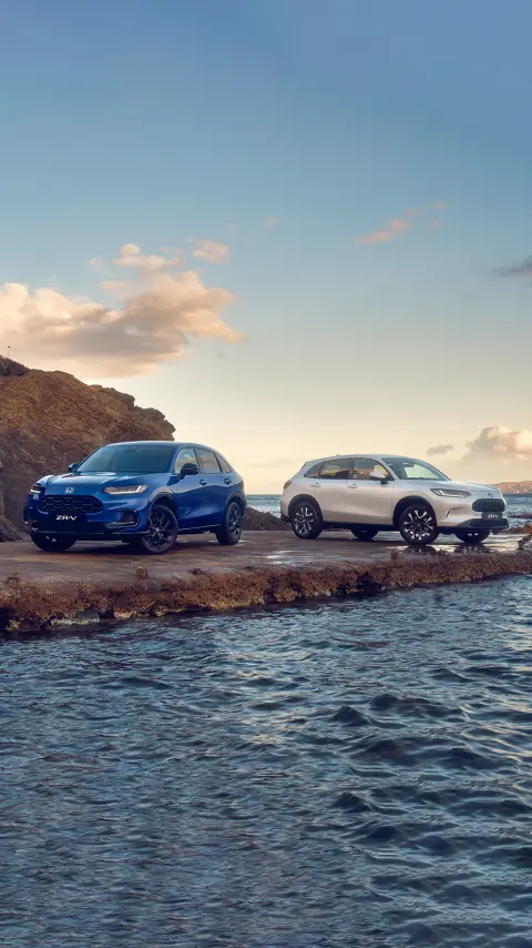 Zwei ZR-V-Hybrid-Fahrzeuge, 3/4-Frontansicht, abgestellt im Gebirge.