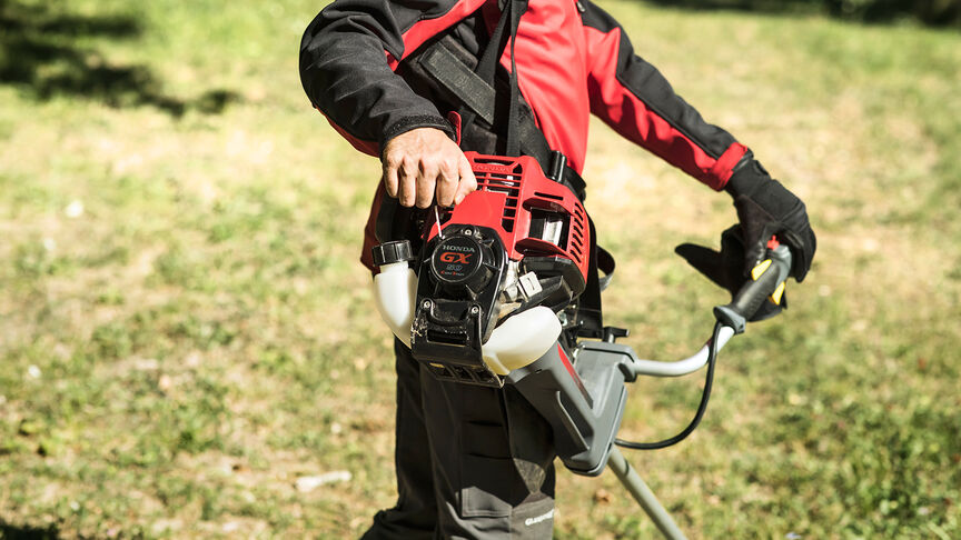 Model mit rückentragbarem Freischneider im Wald.