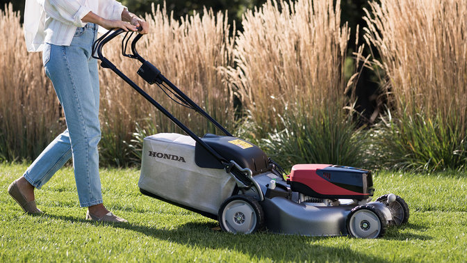 Model demonstrating Honda izy-On lawnmower in garden location.