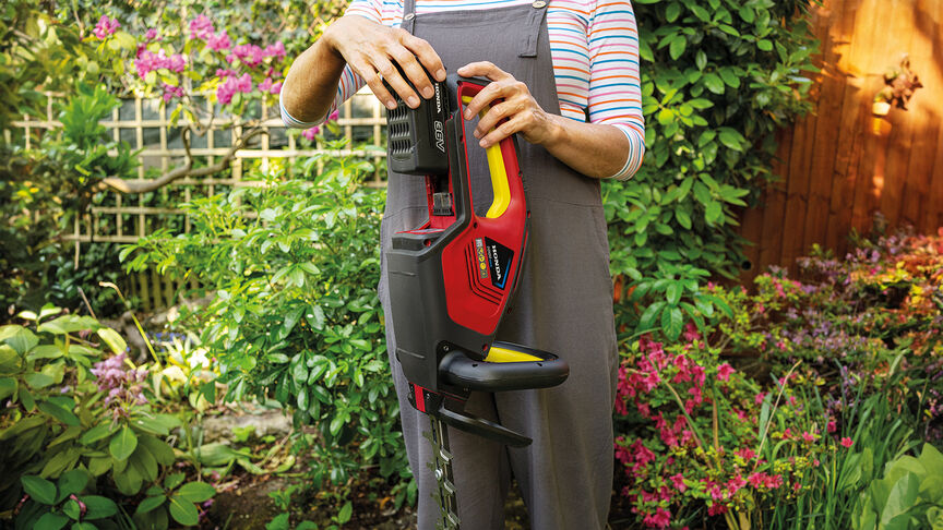 Frau mit Honda Akku-Heckenschere beim Trimmen einer Hecke im Garten.