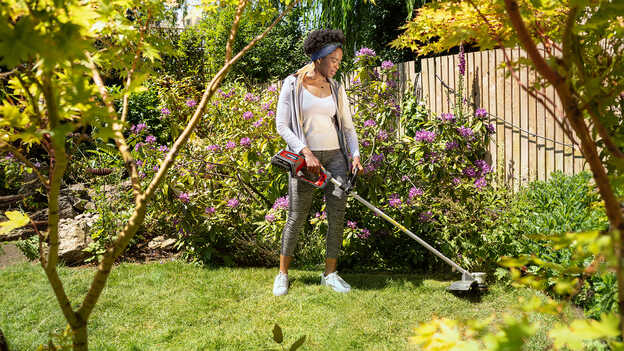 Frau mit einem Honda Akku-Rasentrimmer in einem Garten.