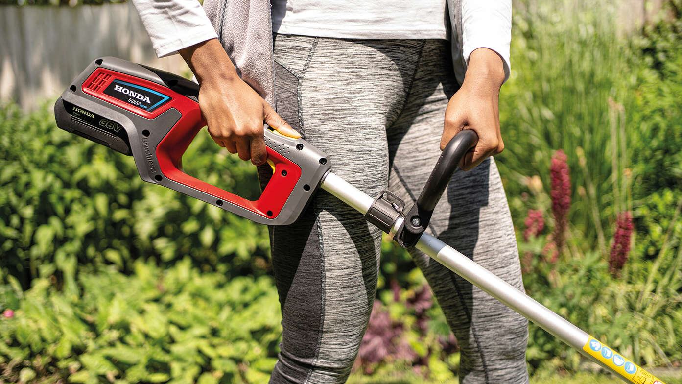 Frau mit Honda Akku-Rasentrimmer in einem Garten, Nahaufnahme.