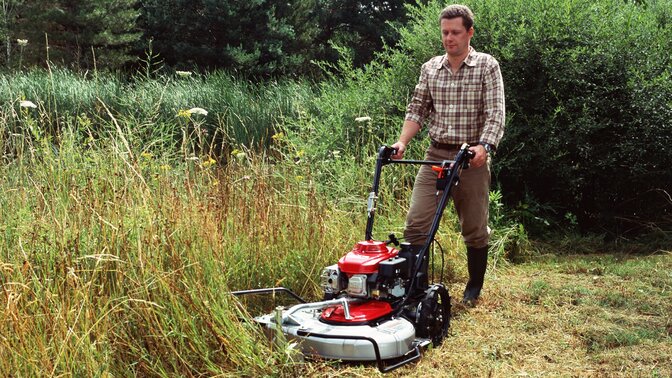 Wiesenmäher in 3/4-Frontansicht, nach links weisend, Verwendung nach Modell. Gartenumgebung.
