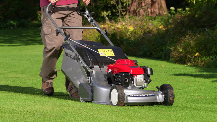 Ein Mann in einem Garten, der mit einem Honda HRD-Rasenmäher Gras mäht.