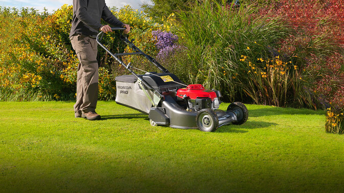 Ein Mann mit einem Honda HRH-Rasenmäher beim Mähen von Gras in einem Garten