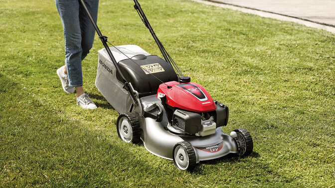 Eine Frau mit einem Honda IZY Rasenmäher beim Mähen von Gras in einem Garten