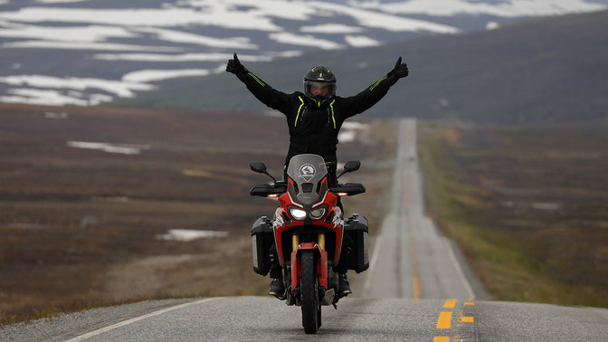 Fahrer auf einer Honda Africa Twin mit hochgestreckten Armen auf den Straßen am Nordkap.