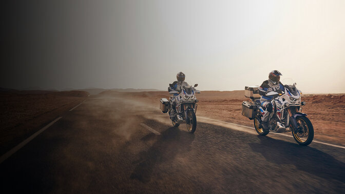 CRF1100 Africa Twin Adventure Sports mit Fahrer auf einer Wüstenstraße, 3/4-Frontansicht. 