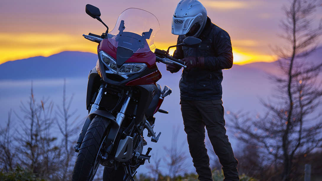 VFR800X, abgestellt in einer Landschaft, daneben der Fahrer.