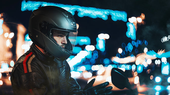 Helm Honda Kabuto, Aeroblade V – mattschwarz – überlagert, 3/4-Frontansicht rechts, auf dem Kopf eines Motorradfahrers, in der Stadt bei Nacht
