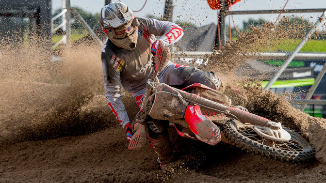 Frontansicht eines Honda Cross-Motorrads mit Fahrer, durch Schlamm rutschend.