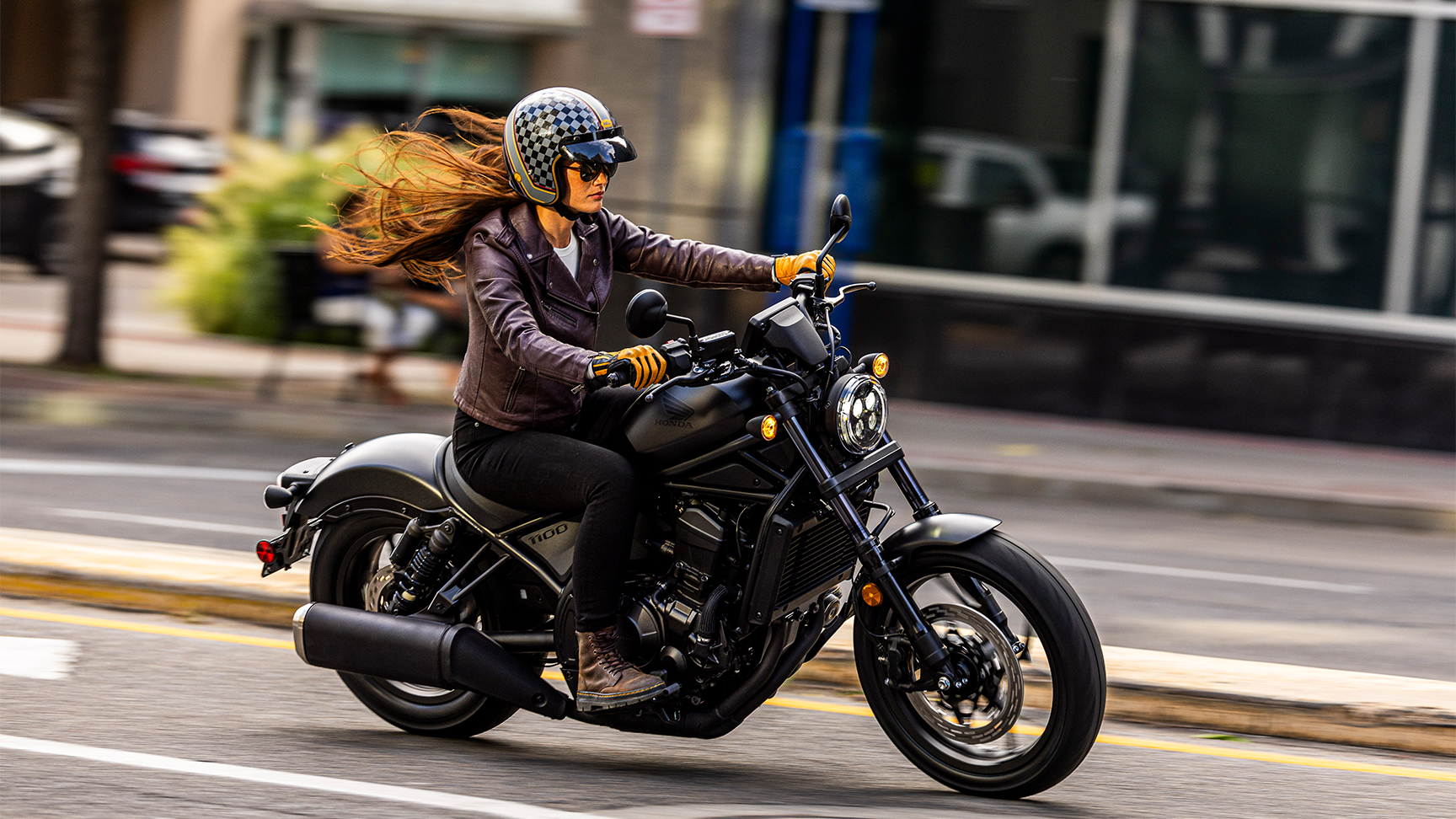 CMX1100 Rebel auf einer asphaltierten Straße in der Stadt mit einer Fahrerin, die eine Lederjacke und einen Jethelm trägt