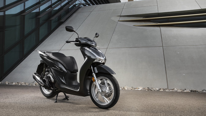 Honda Sh125i mit Topcase und Windschild auf der Straße.
