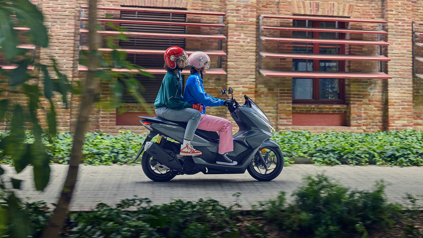Seitenaufnahme von Models, die den PCX125 in der Stadt fahren.