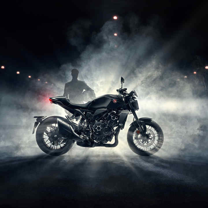 Honda CB1000R Black Edition von rechts, Fahrer steht bei nächtlichem Nebel hinter dem schwarzen Motorrad