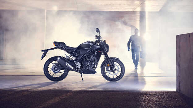 Honda CB300R, Seitenansicht, abgestellt in einer Garage und Mann, der auf das Motorrad zugeht.