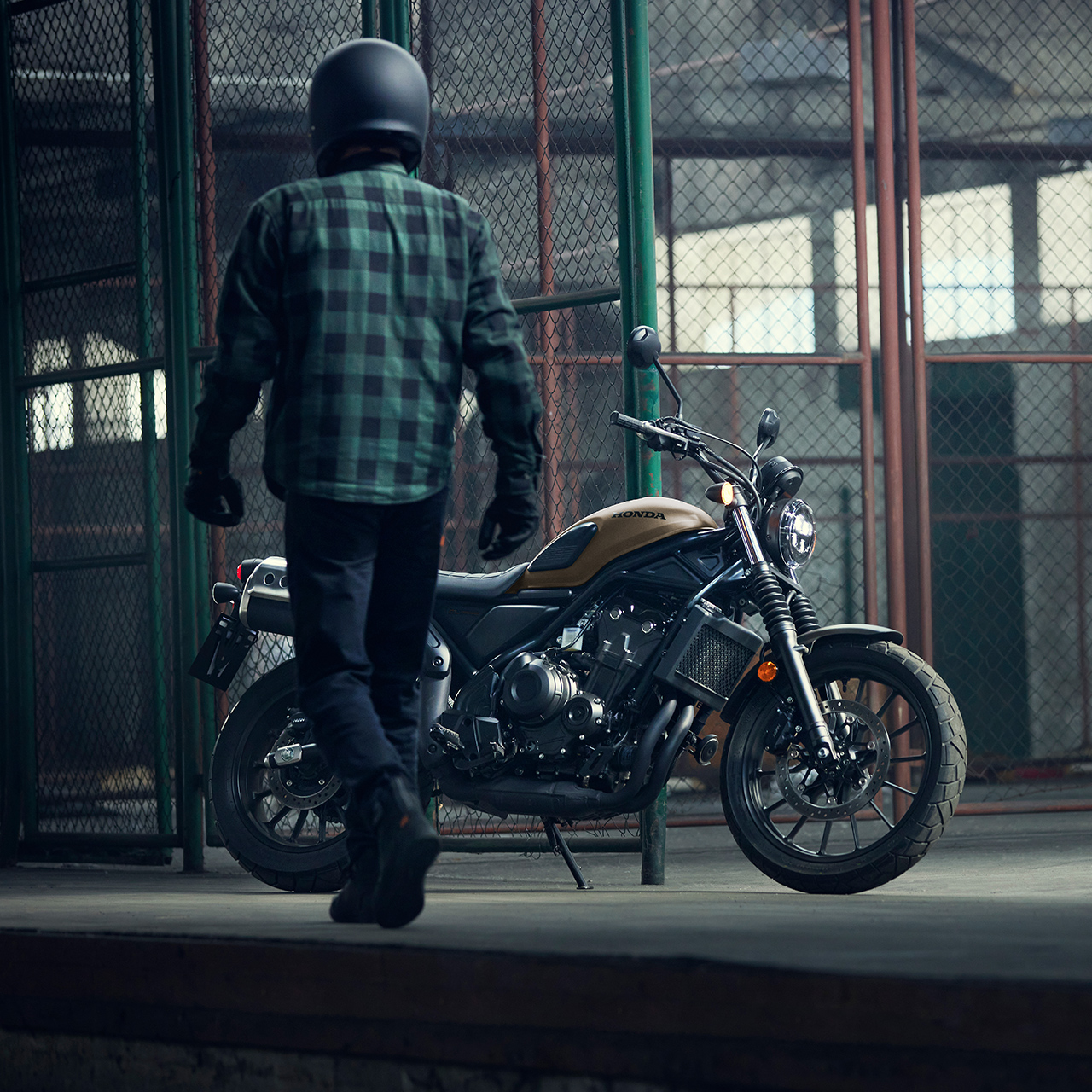 Ein Fahrer geht entlang eines geparkten Honda CL500 Motorrads in einer Lagerhalle.