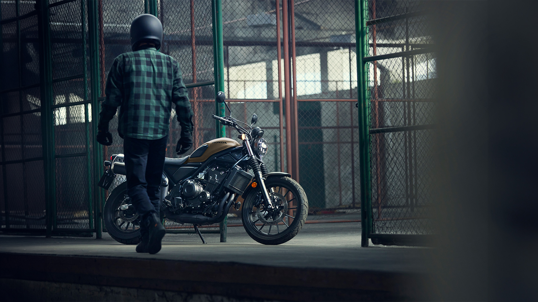 Ein Fahrer geht entlang eines geparkten Honda CL500 Motorrads in einer Lagerhalle.