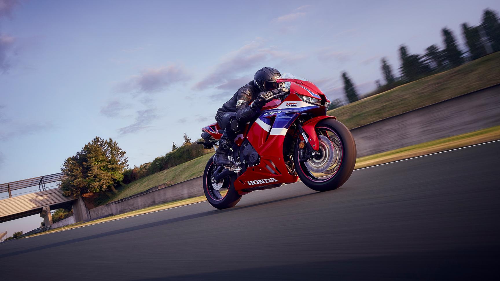 CBR600RR mit Fahrer in einer Kurve auf einer Rennstrecke bei Sonnenuntergang.