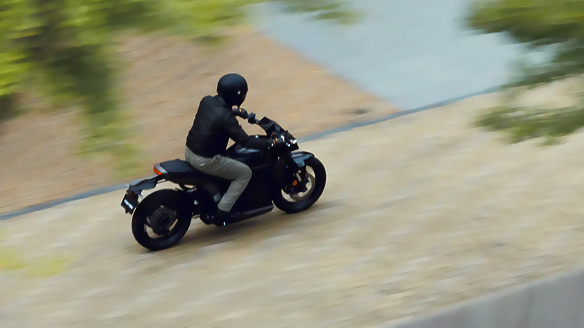 Eine schwarze Honda WN7 auf einer kurvigen Straße in der Nähe eines Gewässers, aufgenommen mit einem verschwommenen Hintergrund der auf eine hohe Geschwindigkeit hindeutet. 